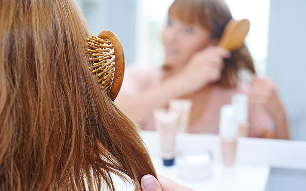 Woman worried about hair loss brushing her hair and looking in the mirror